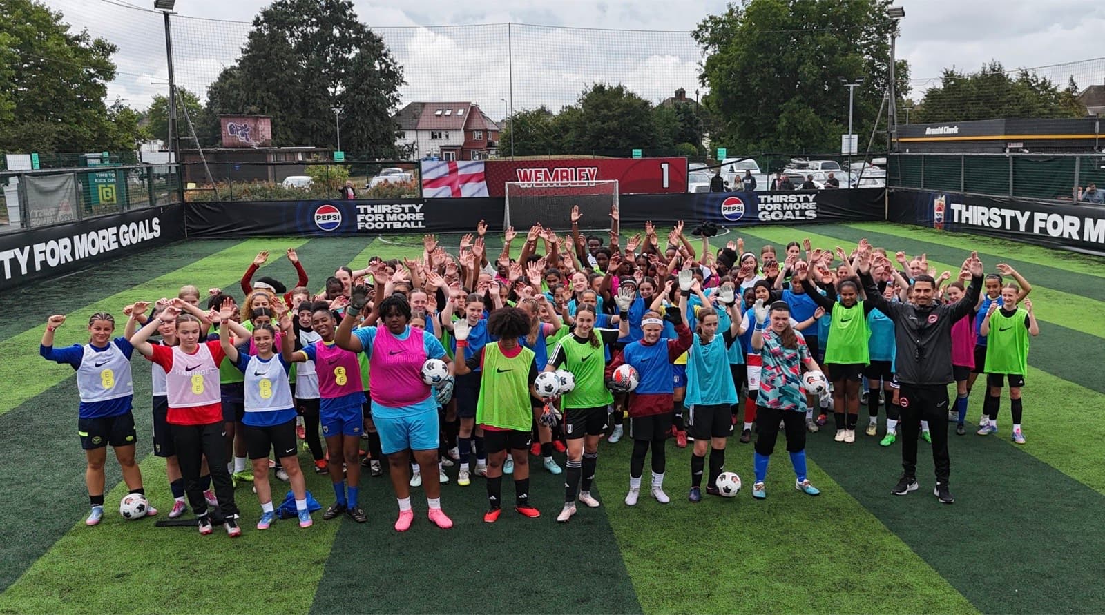 Young female footballers celebrating with arms raised on a cage pitch at a Top Baller talent identification event at Wembley